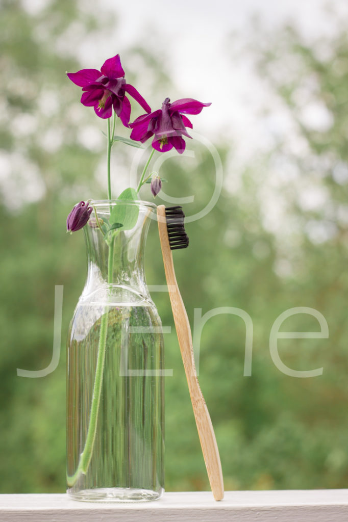 Tandborste i bambu står lutad mot en glasvas med blommor av akleja.